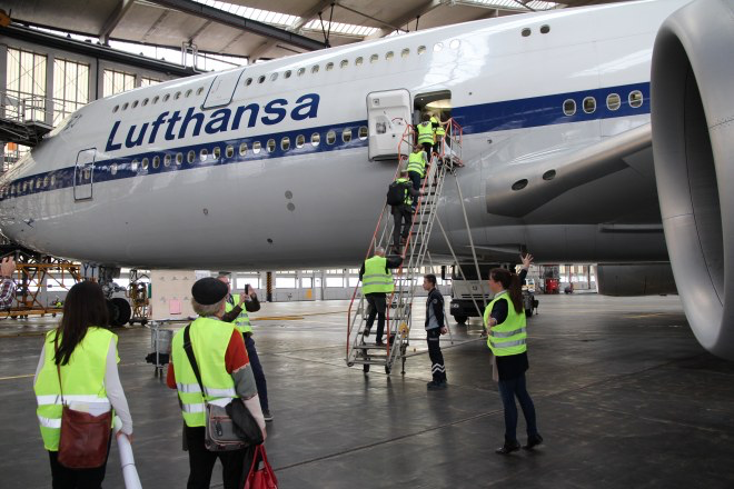 Die Teilnehmerinnen des Botschaftertreffens besteigen über eine mobile Rolltreppe eine Boing in der Wartungshalle